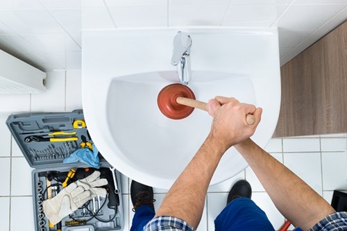 plumbing service engineer unblocking sink with plunger and tools